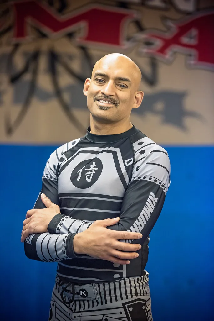 Karmjeet Manhas, founder of Kaiten MMA, in a rash guard in front of the gym wall